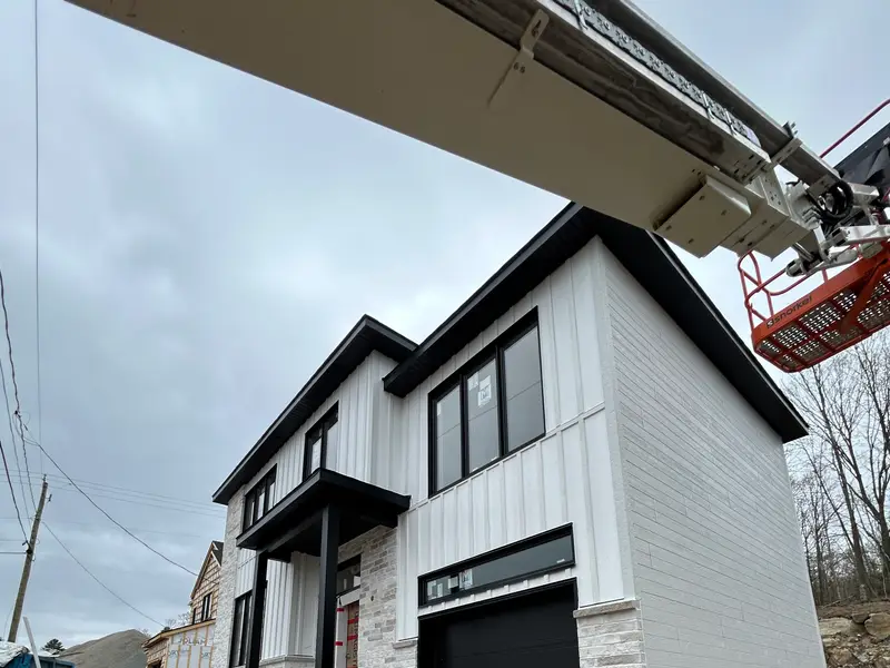 Maison de deux étages avec revêtement blanc vertical, pierre et porte de garage noire
