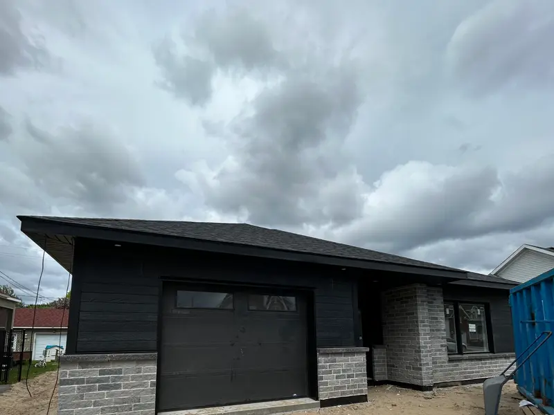 Bâtiment avec revêtement noir, pierre et grande porte de garage