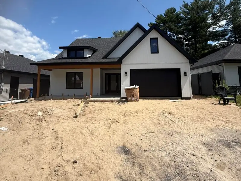 Maison neuve blanche avec porte de garage noire et poutres de bois